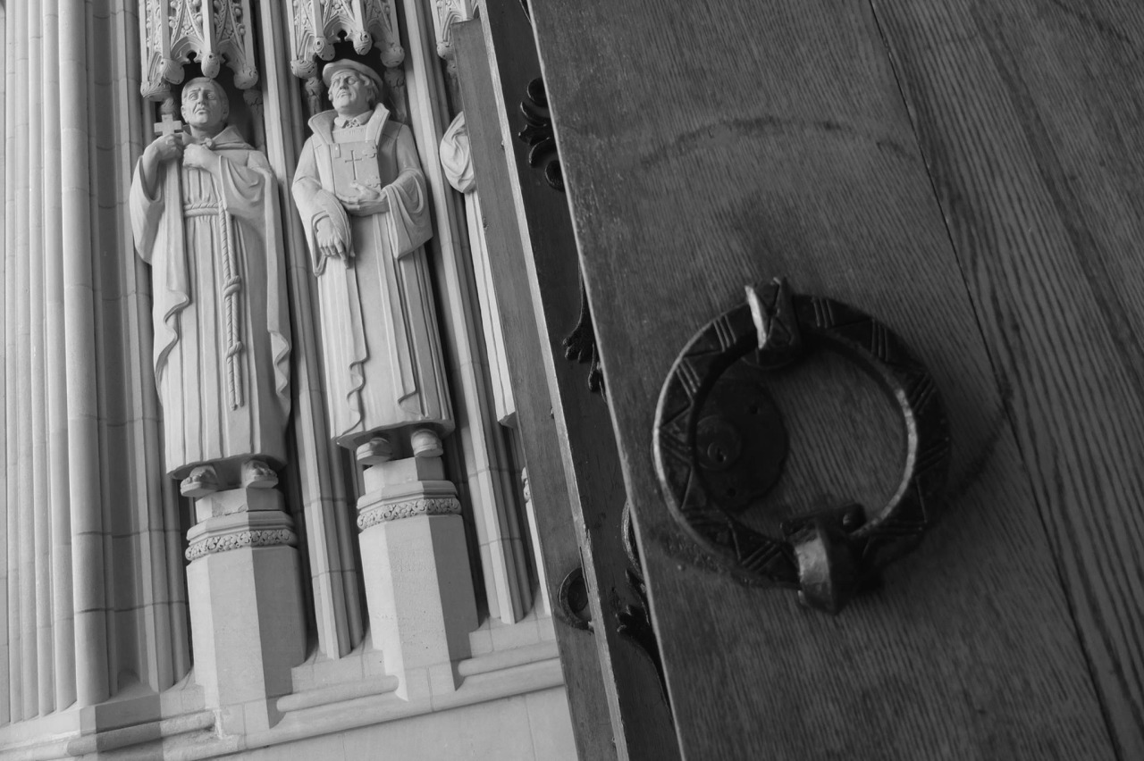 black and white photo of Duke Chapel's heavy wooden doors and statues