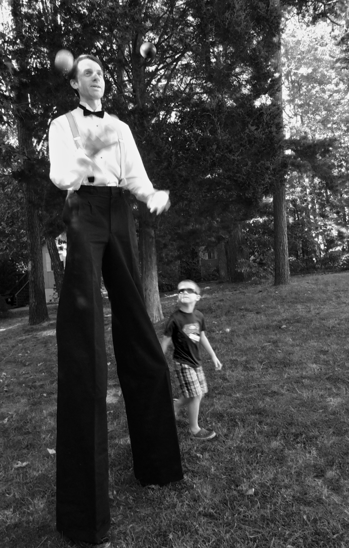 man on stilts juggling with little boy watching
