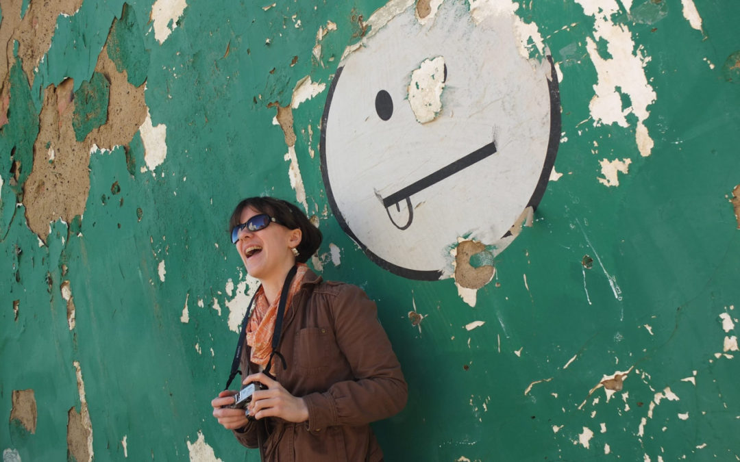 photo of a girl sticking her tongue out leaning against a wall with a smiley face graphic sticking its tongue out