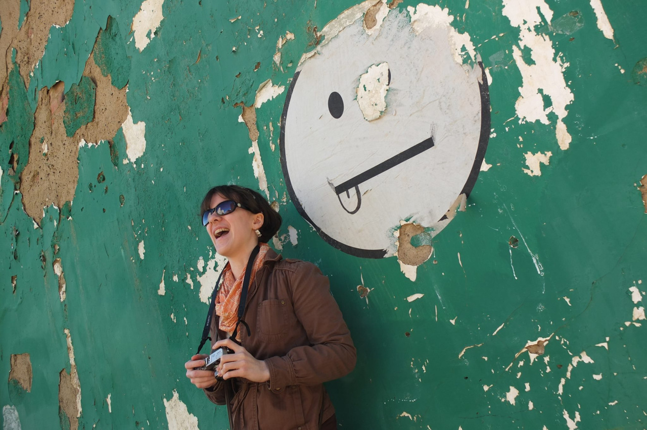 photo of a girl sticking her tongue out leaning against a wall with a smiley face graphic sticking its tongue out