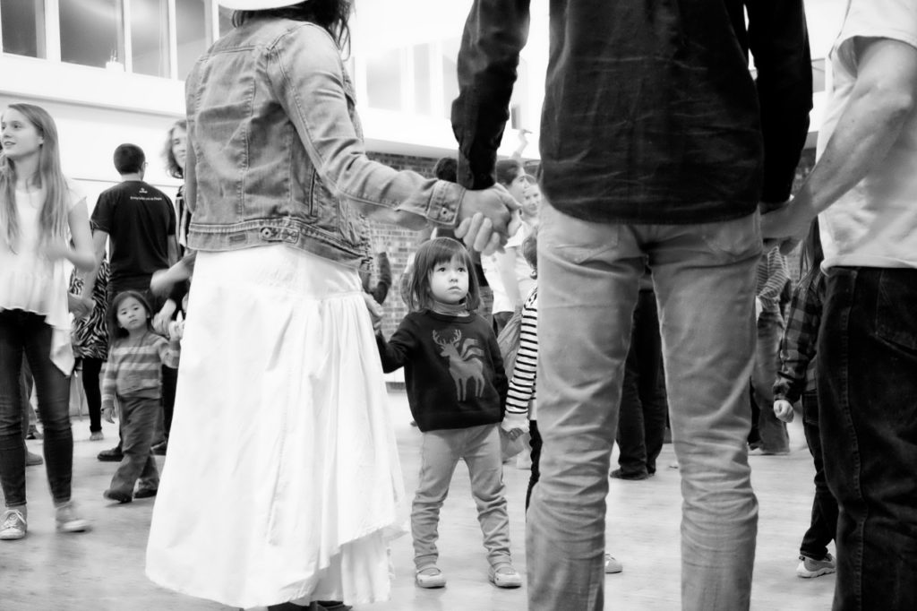 black and white photo at a country dance showing a little girl at the level of adult's legs