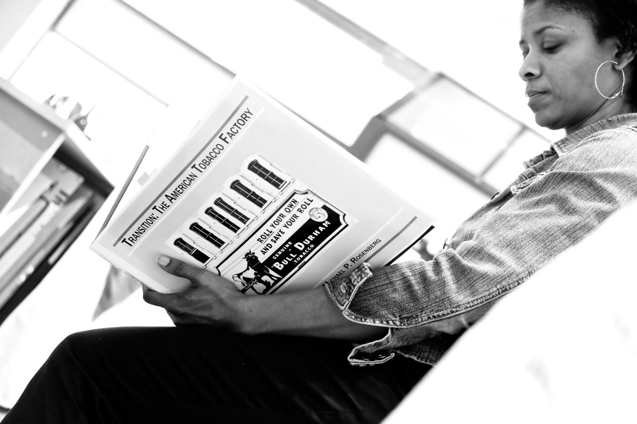 close up image of a woman reading a book of Durham images called 'Transitions: The American Tobacco Factory'