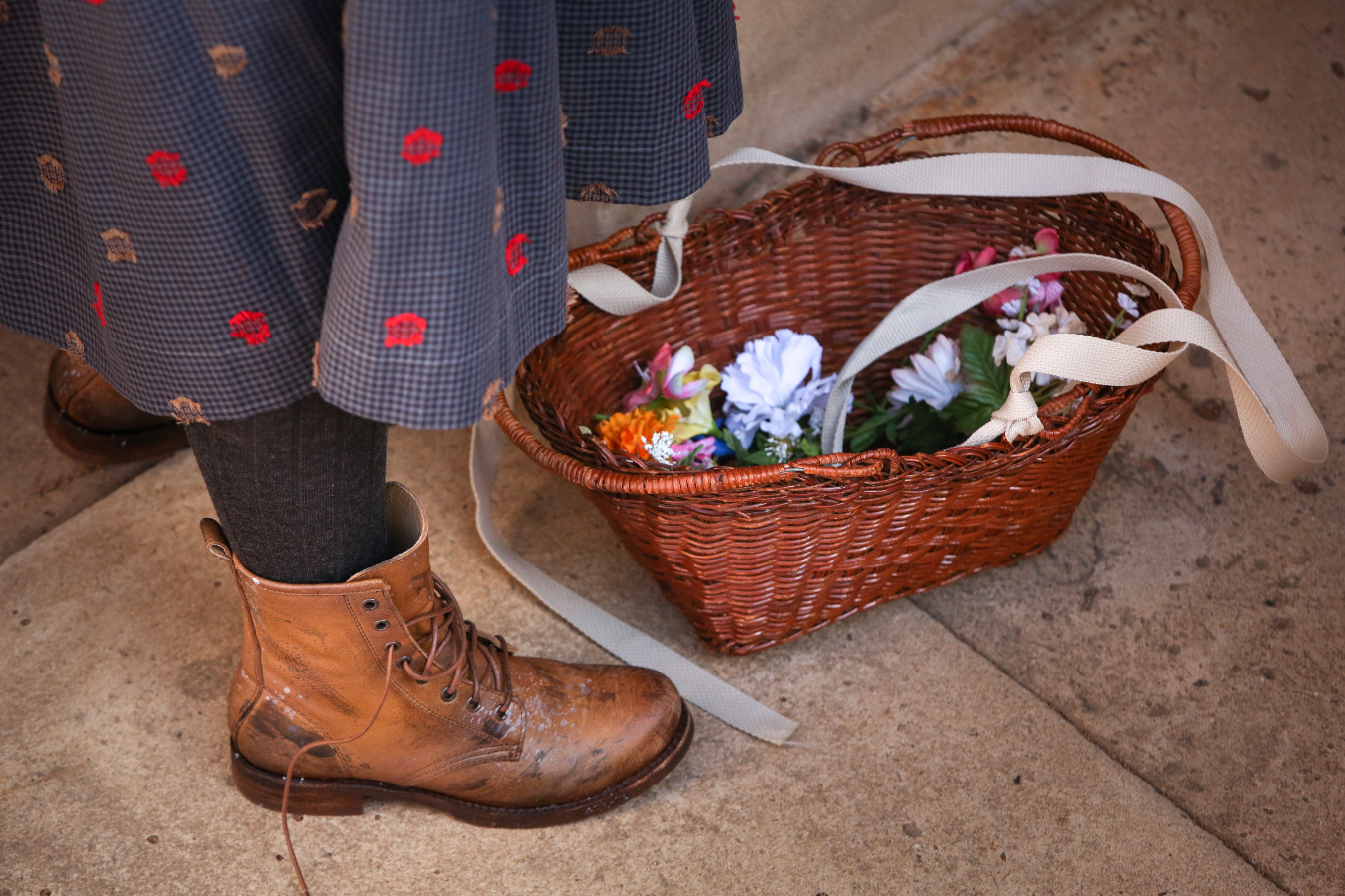 detail photos of actor in a rough skirt 1900's boots with a flower basket at her feet