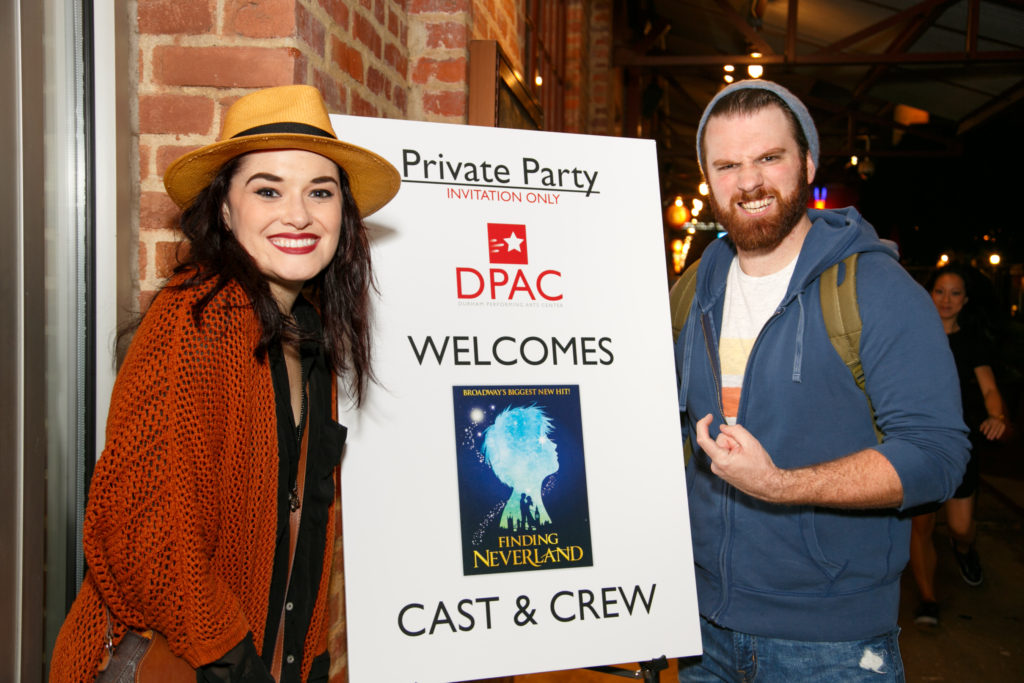 Photo of actor making 'hook' gesture with his hand and actress beside 'Finding Neverland' cast party sign