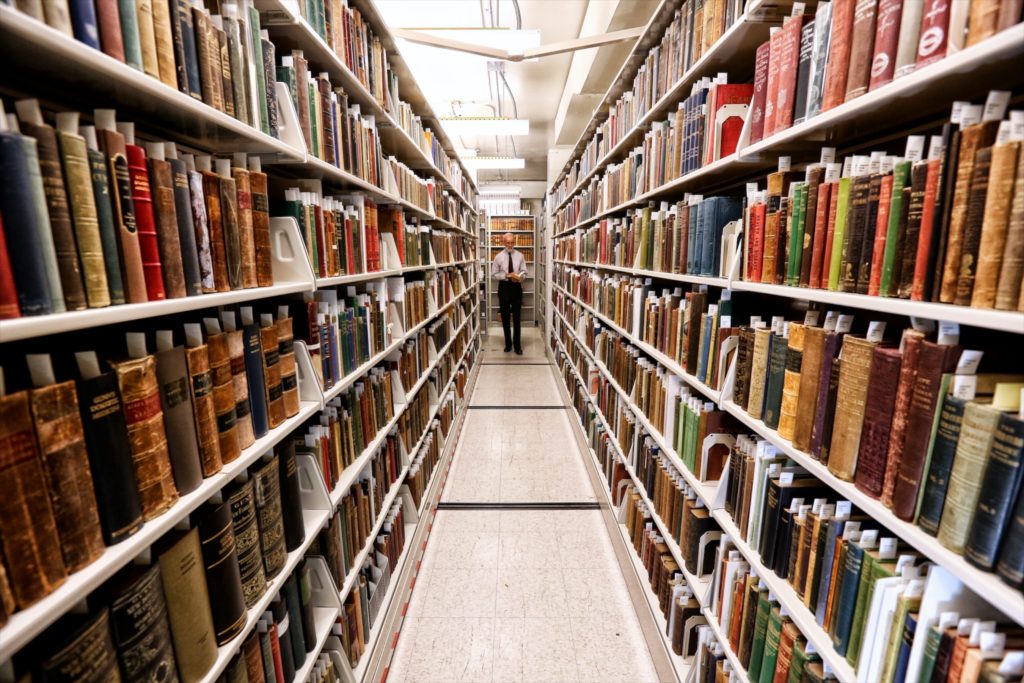 wide view of books on either side in a bright room with an old man far to the back in the center of the image