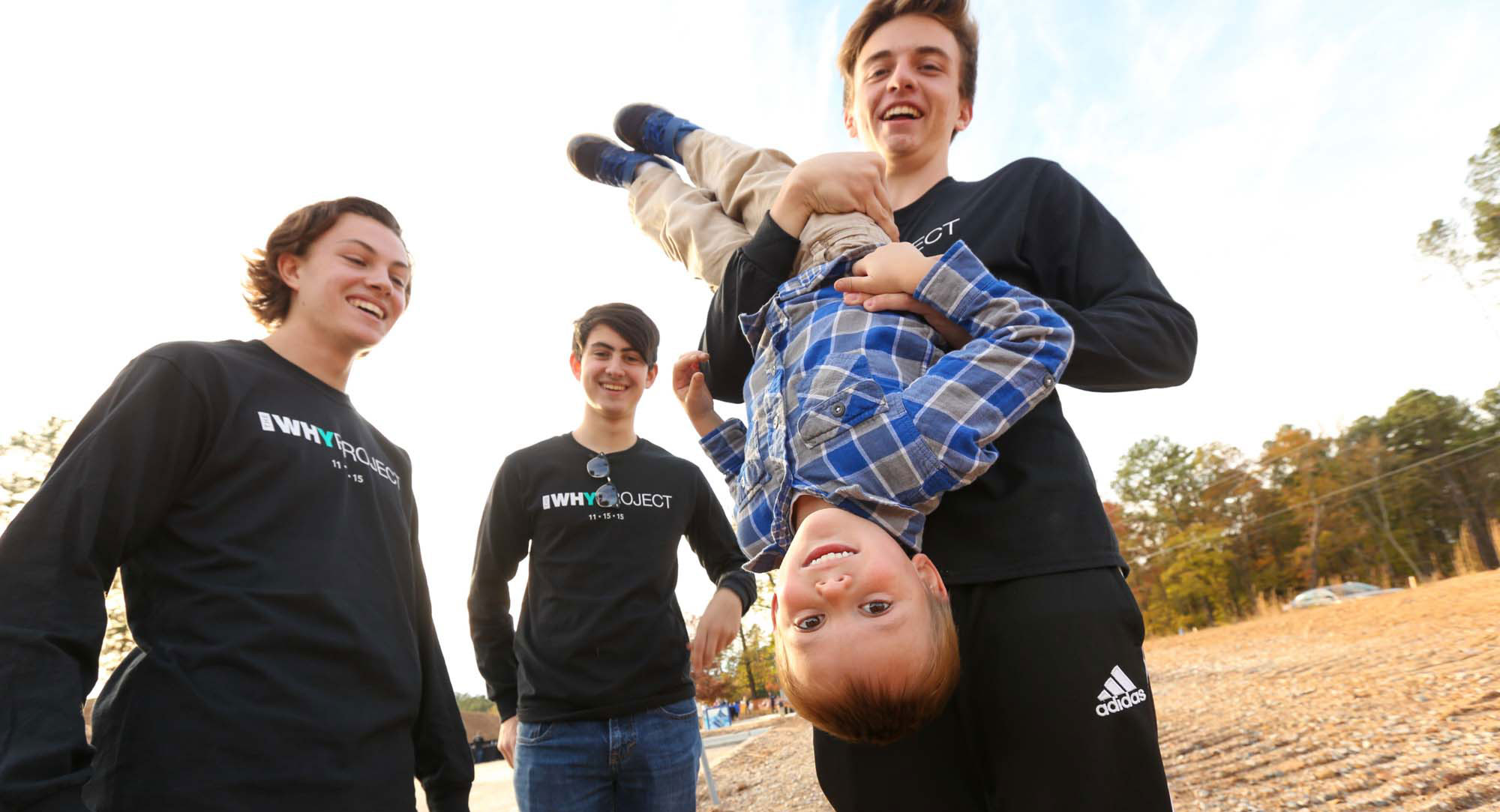 younger boy smiling, being held upside down by an older boy and girl