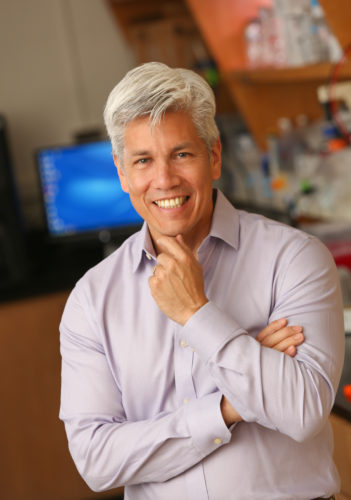 portrait of a man with a science lab soft behind him