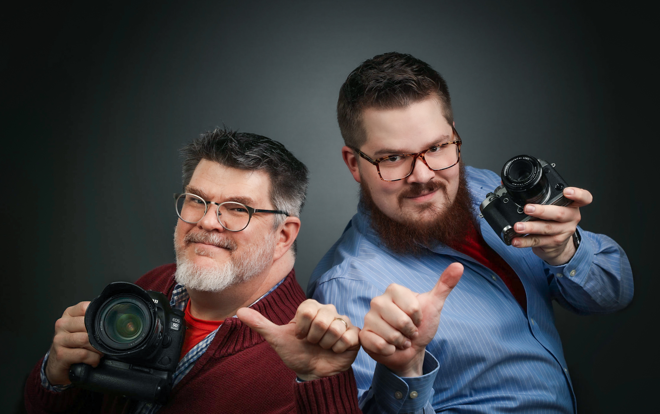 Ken Huth in a suit and with a camera in-hand, leaps into the air for joy and looks a bit silly