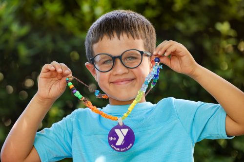 photo of young boy smiling, holding a YMCA medal proudly