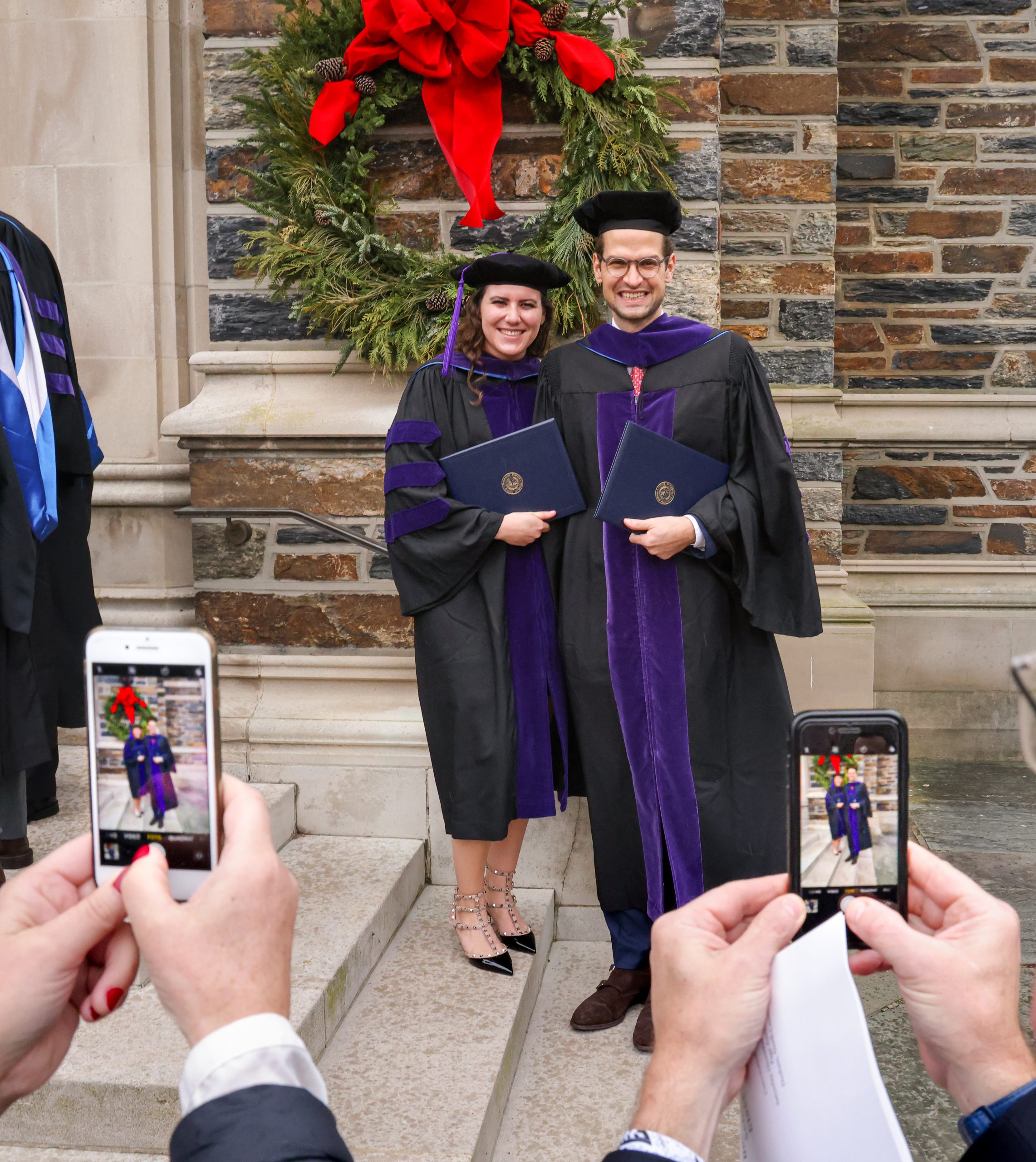 two people's hands holding cell phone cameras snap happy graduate couple's photo
