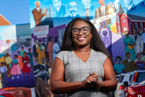 photo of a smiling black woman in front of a colorful civil right mural