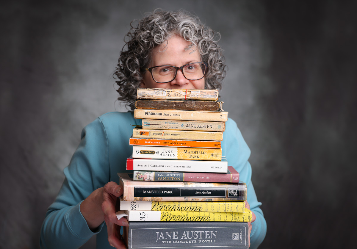 photo of a woman with curly hair holding a large stack of Jane Austen books