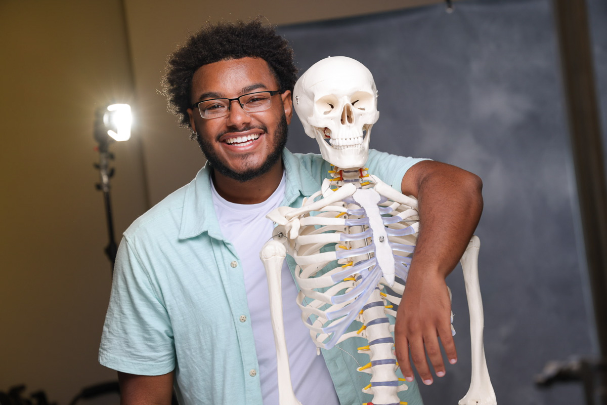 young man smiling with his arm around a medical skeleton