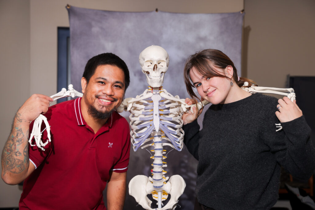 Rajha Tahir and Claire Hambrick having fun with a medical skeleton with its arms around their shoulders