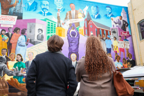 Two people stand in front of the colorful Durham civil rights mural.