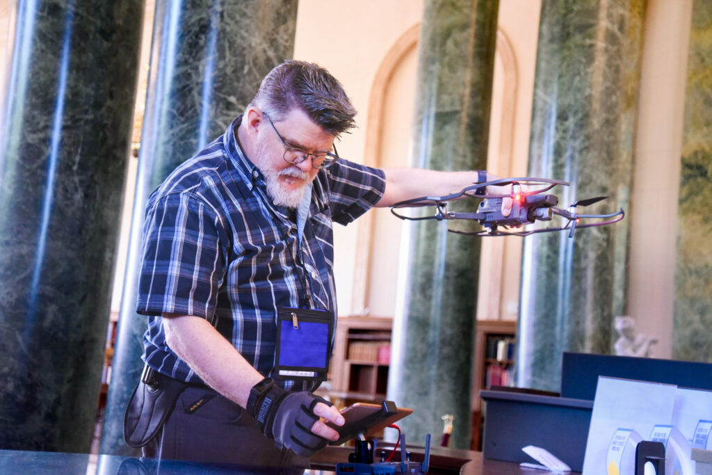 Ken Huth looks at an iPad while holding a drone for launch in historic Wilson library at UNC