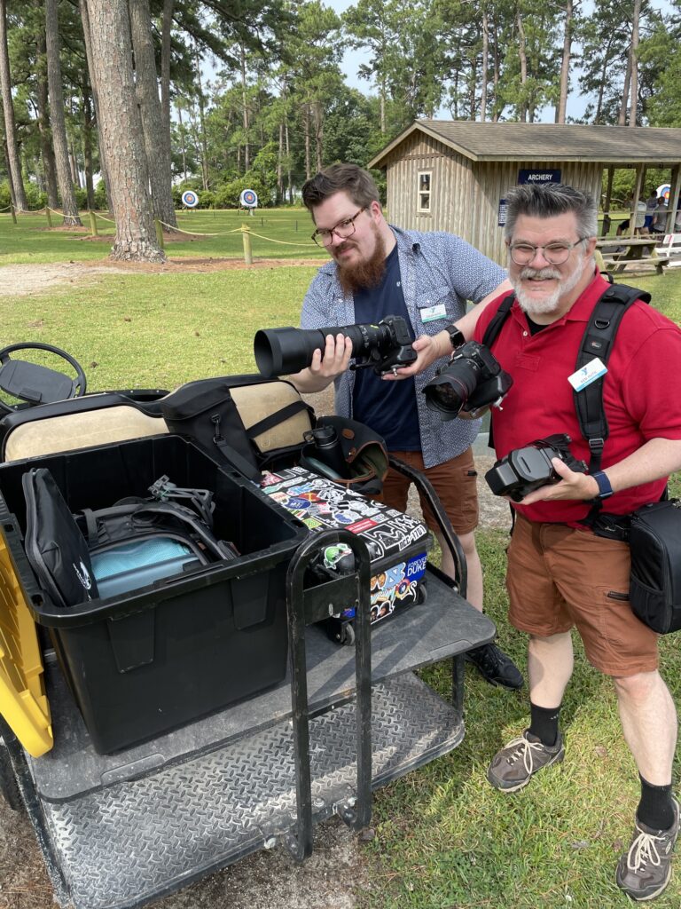 Ken and Colin Huth in summer shorts with a large golf cart full of photo equipment at at YMCA camp
