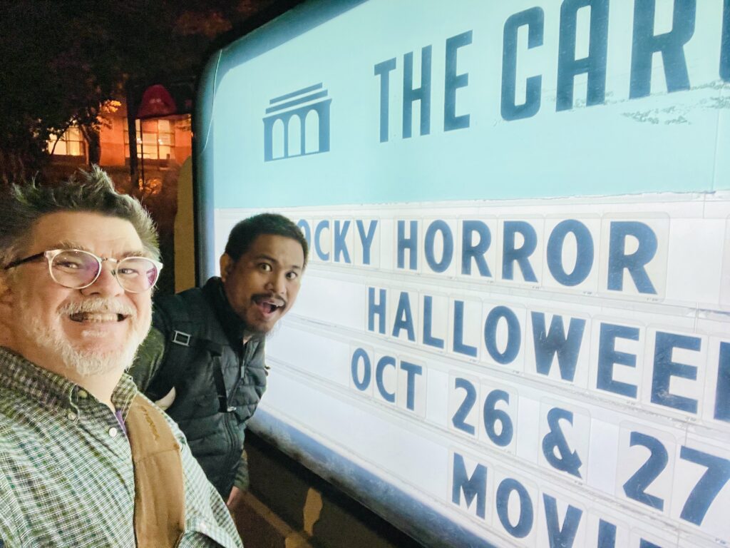 Ken Huth and Rajha Tahir smile for the camera very close to the Carolina Theatre Durham signing saying Rocky Horror Halloween event