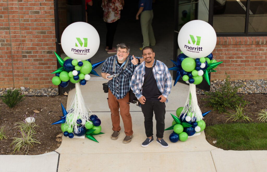 Ken Huth and Rajha Tahir are photographed by drone smiling, with larger white balloons for client Merritt