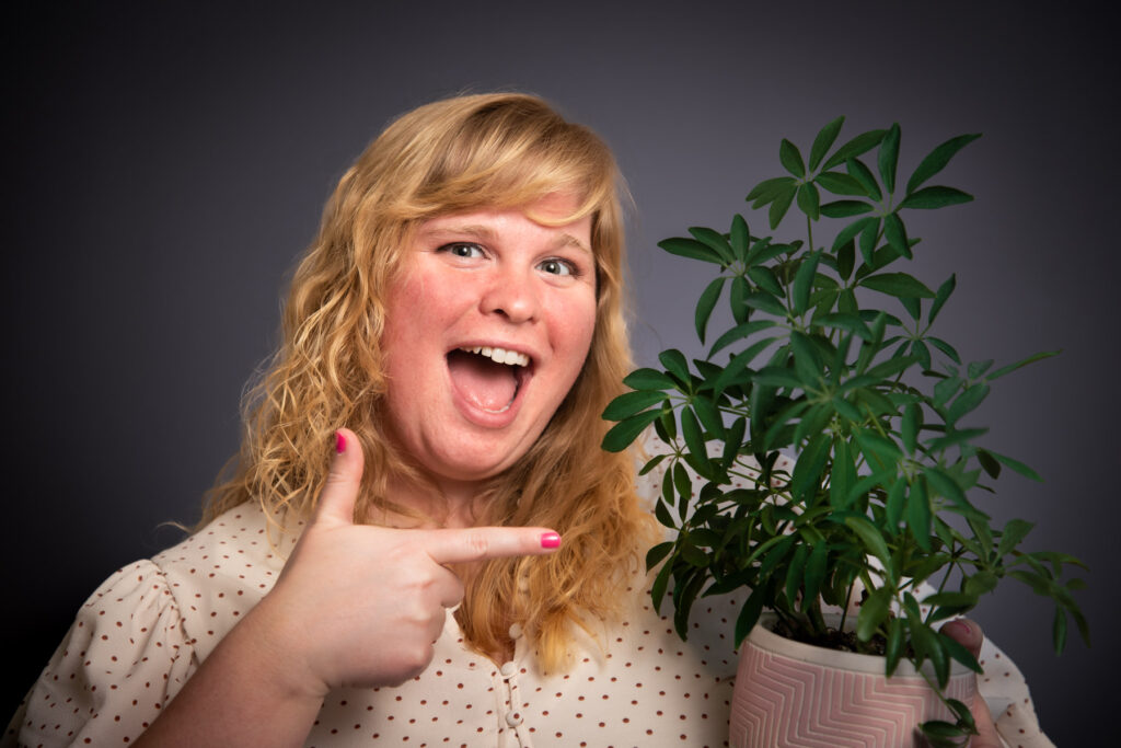 Lizzie Potter with a huge laughing smile points to her very healthy potted plant