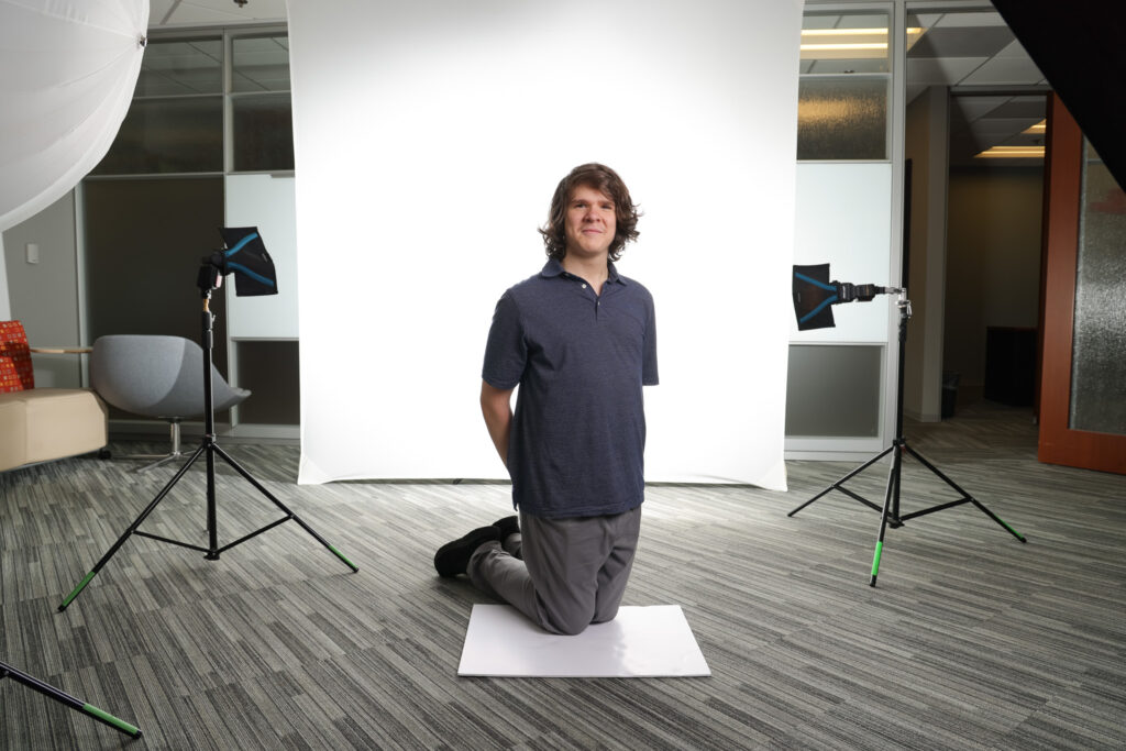 Oliver Huth young photo assistant, kneels surrounded by photo lights and a white background for a light test on how light will hit children for a photo