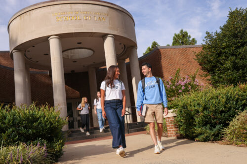 image of college age man and woman walking in front of the columned entrance to UNC Law School. They are wearing UNC Law shirts