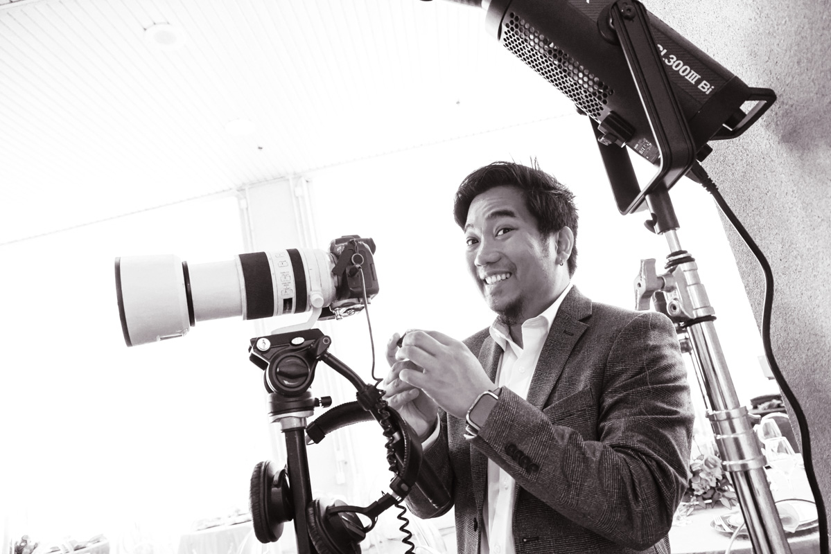 Monochrome image of a young Filipino man (Daryl Mullasgo) in a suit with a camera on tripod nearby