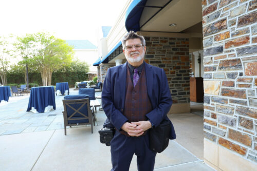 man standing looking at the camera with tables and a brick wall behind him