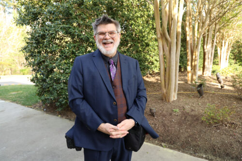 man standing looking at the camera with darker trees behind him