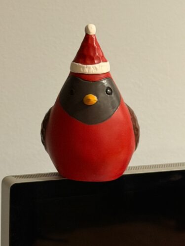 photo of a wooden bird statue with a Santa hat. The room color is yellow-ish and the one eye of the bird looks dark